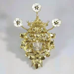 Broche "Rosa acorazonada coronada" en plata de ley chapada en oro con esmaltes y un pequeño relicario con un trozo de manto de la Virgen del Rocío de Almonte. Basado en modelos de joyería antigua (Joyería El Oribe, 2023). Foto extraída de las redes sociales de la Hermandad de la Tercera Caída.